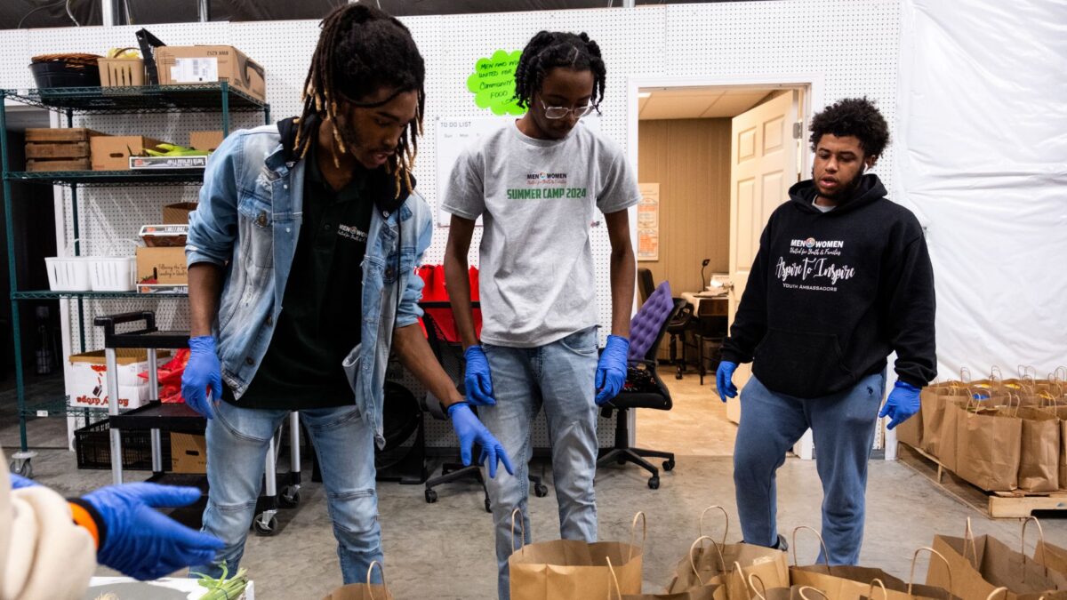 Three young men stand in front of empty produce bags in a warehouse