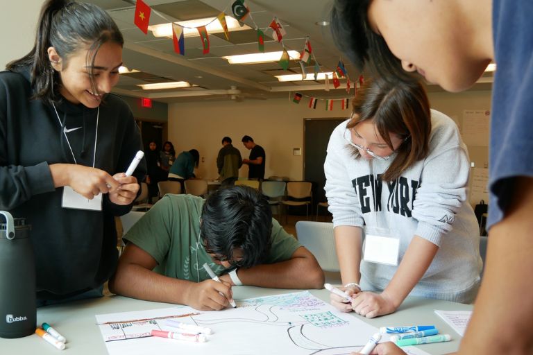 High school students work together at a table, smiling and creating a poster