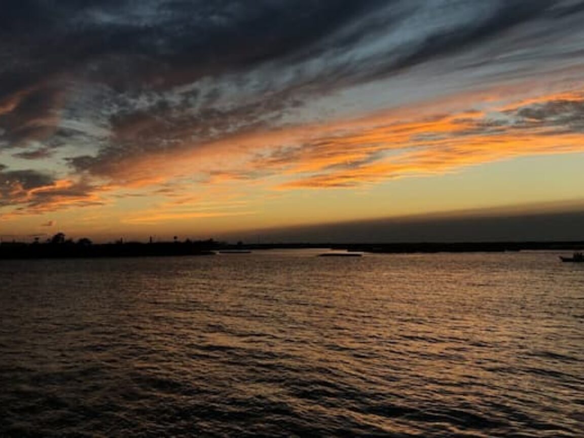 Sunset over a calm body of water with dark clouds and orange hues in the sky.