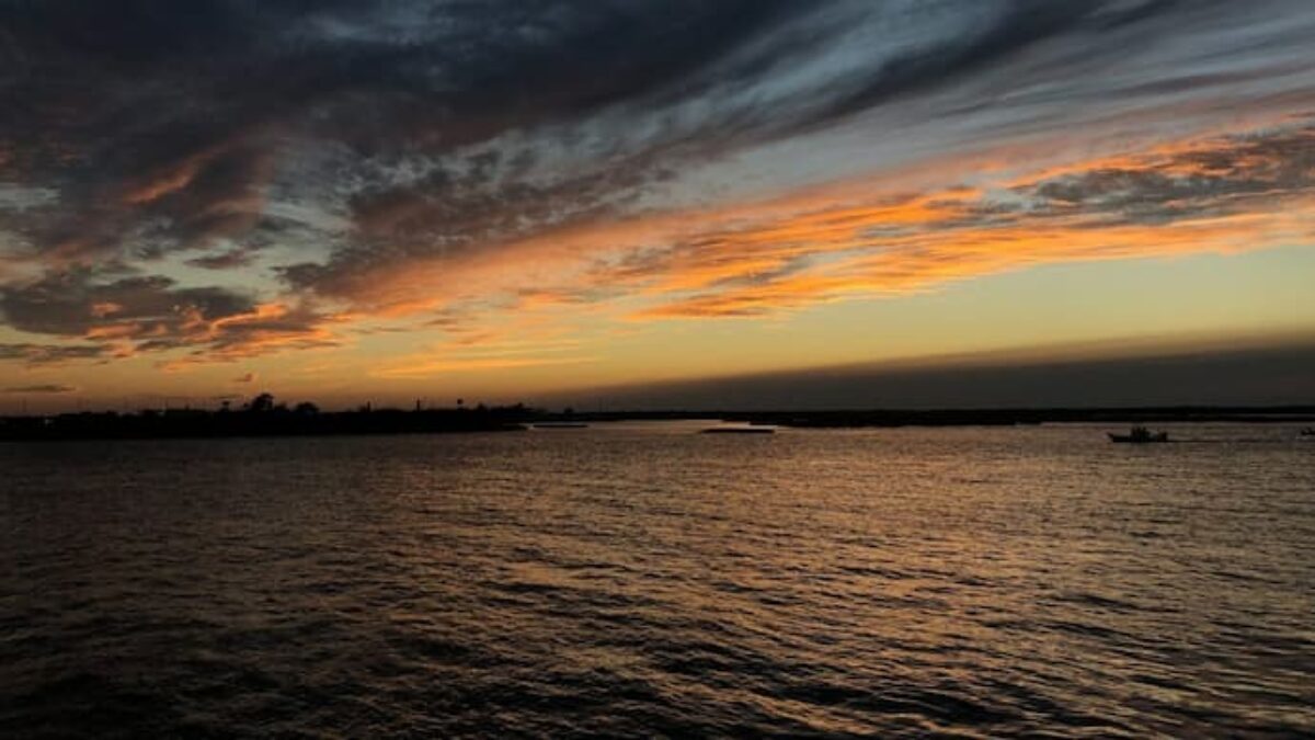Sunset over a calm body of water with dark clouds and orange hues in the sky.
