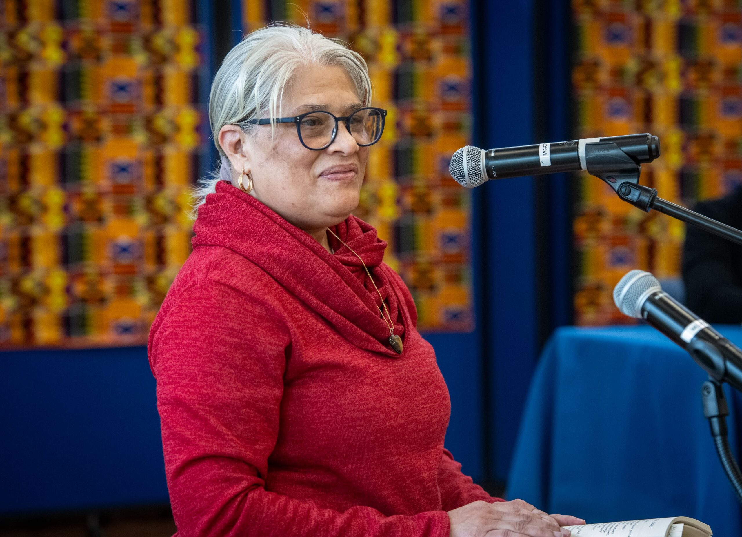 Nicola Karesh stands in front of a microphone wearing a bright red sweater