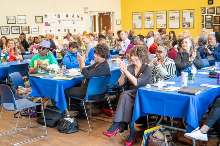 A roomful of diverse people clapping and smiling