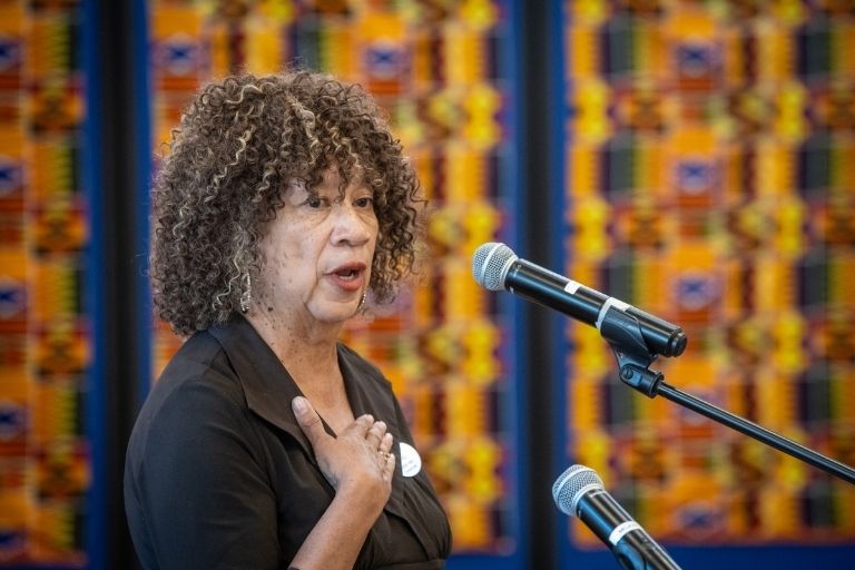 Woman speaks into a microphone with colorful cloth behind her