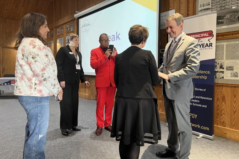People networking at a school leadership event, with a presentation screen and Principal of the Year banner.