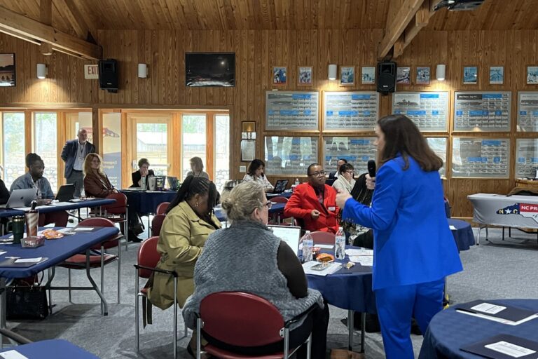 Workshop meeting in a wood-paneled room, with a speaker addressing seated attendees at round tables.