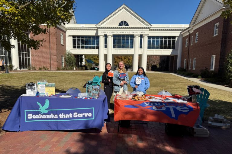 Students at campus outreach tables in front of college buildings