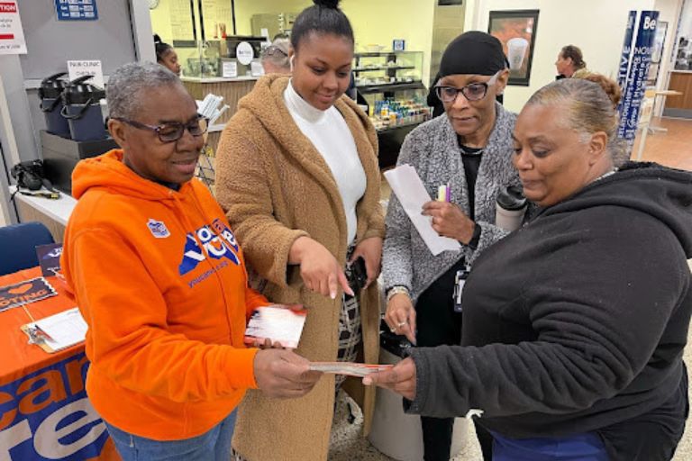 Four women reviewing flyers at a community event table indoors.
