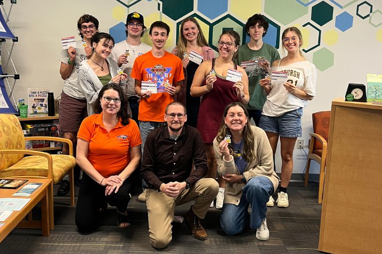 Group of people posing indoors, holding small prizes and cards in a colorful lounge area.