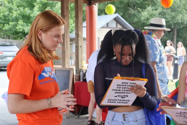 Volunteer helps a young woman register to vote at an outdoor event.