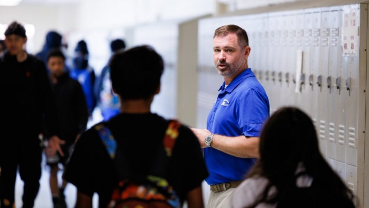 Principal speaking to students in a school hallway beside lockers
